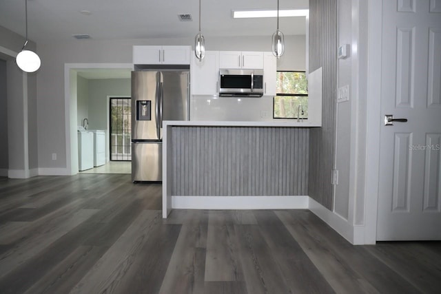 kitchen featuring white cabinetry, hanging light fixtures, dark wood-type flooring, stainless steel appliances, and washing machine and dryer