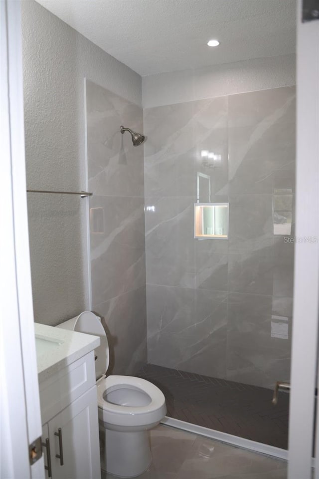 bathroom featuring tiled shower, a textured ceiling, vanity, and toilet