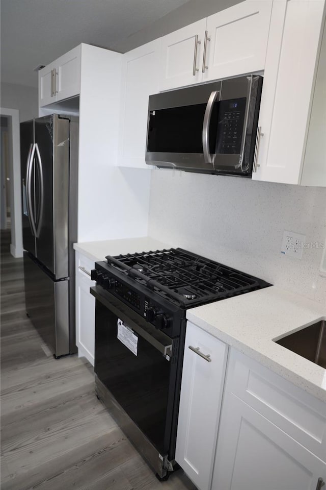 kitchen with white cabinets, appliances with stainless steel finishes, light hardwood / wood-style flooring, and light stone counters