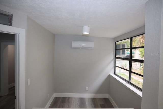 empty room with an AC wall unit, dark wood-type flooring, and a textured ceiling