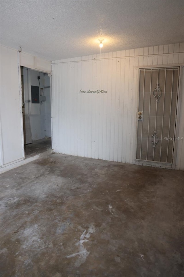 empty room with concrete flooring, a textured ceiling, and electric panel