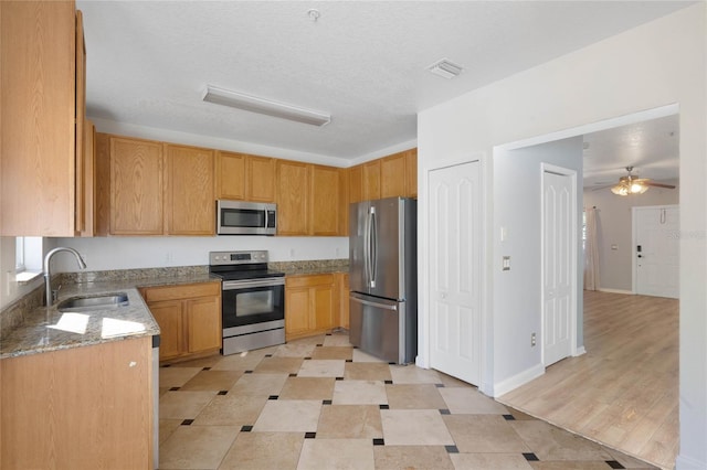 kitchen with sink, light hardwood / wood-style flooring, ceiling fan, light stone countertops, and appliances with stainless steel finishes