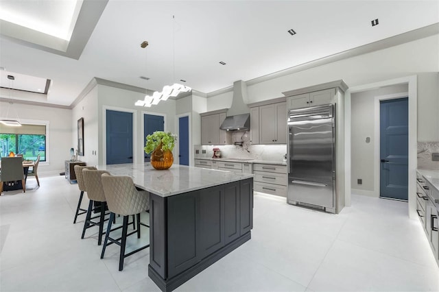 kitchen featuring gray cabinets, a spacious island, wall chimney exhaust hood, and built in fridge