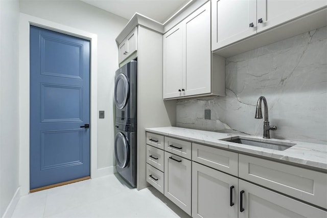 laundry area featuring cabinets, stacked washer / dryer, and sink