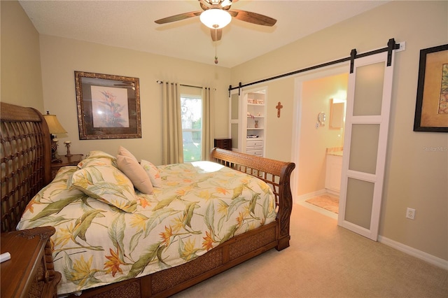 carpeted bedroom with ceiling fan, connected bathroom, and a barn door