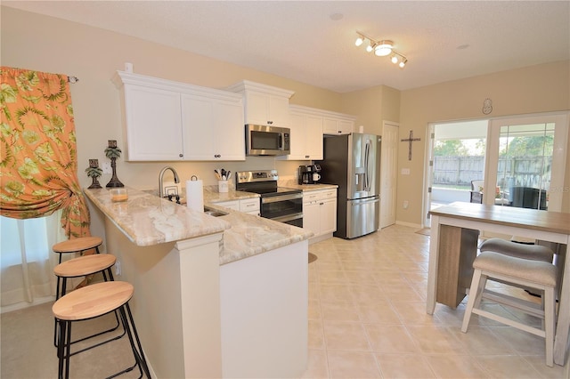 kitchen featuring white cabinetry, a kitchen bar, light stone counters, kitchen peninsula, and stainless steel appliances