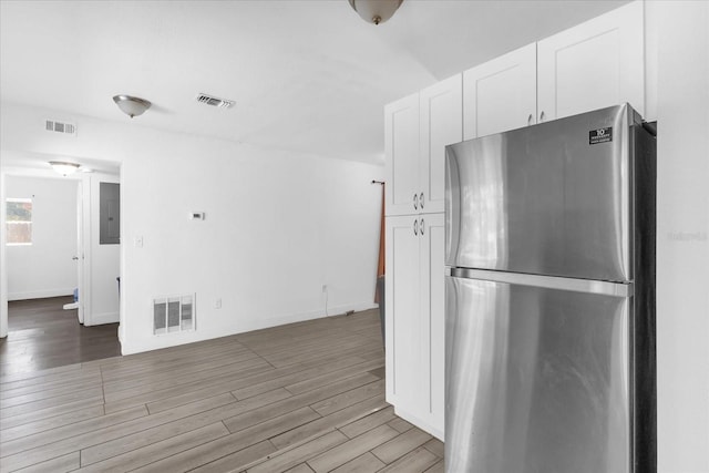 kitchen with wood-type flooring, stainless steel fridge, electric panel, and white cabinets