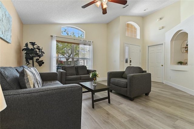 living room with a textured ceiling, light hardwood / wood-style floors, high vaulted ceiling, and ceiling fan