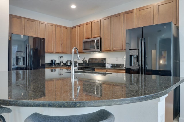 kitchen with sink, dark stone counters, a kitchen bar, a kitchen island with sink, and black appliances