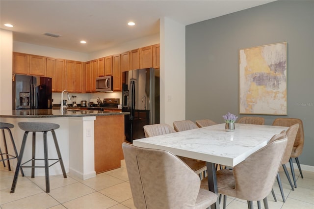 kitchen with sink, an island with sink, a breakfast bar, light tile patterned floors, and black appliances