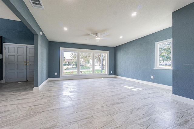 unfurnished room with ceiling fan, visible vents, a textured wall, and a wealth of natural light