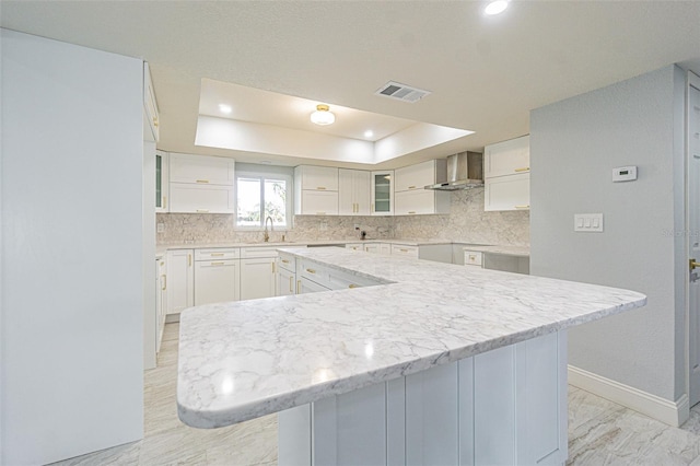kitchen featuring visible vents, a kitchen island, wall chimney range hood, tasteful backsplash, and a sink
