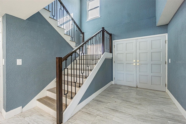 staircase featuring baseboards, a textured wall, a high ceiling, and marble finish floor