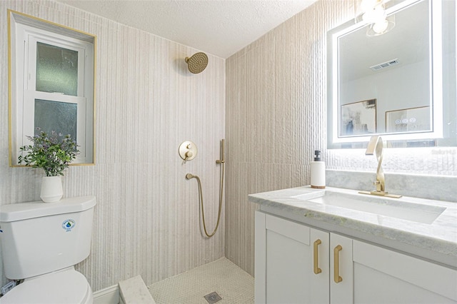 bathroom with vanity, a tile shower, toilet, and wallpapered walls