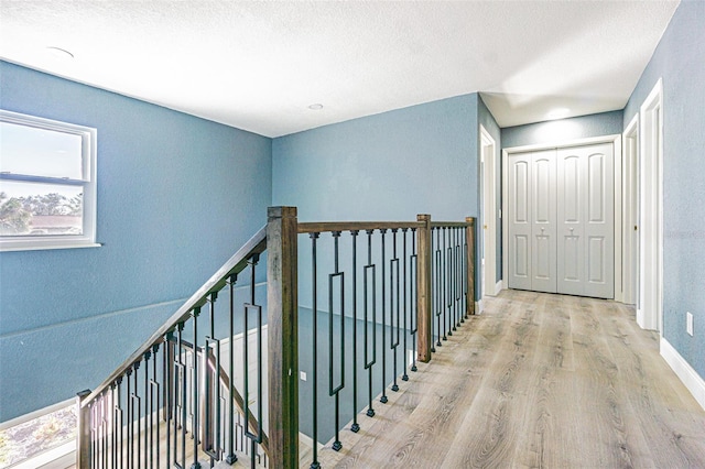 hall with a textured ceiling, wood finished floors, baseboards, an upstairs landing, and a textured wall