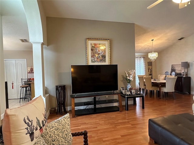 living room with ornate columns, ceiling fan with notable chandelier, vaulted ceiling, and hardwood / wood-style flooring