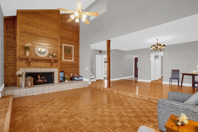 unfurnished living room featuring high vaulted ceiling, a tile fireplace, ceiling fan with notable chandelier, wooden walls, and parquet flooring