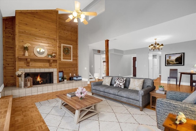 living room featuring ceiling fan with notable chandelier, light parquet floors, wooden walls, a tile fireplace, and high vaulted ceiling