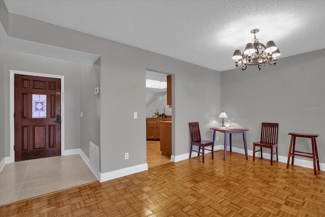 foyer with a textured ceiling, a notable chandelier, and light parquet flooring