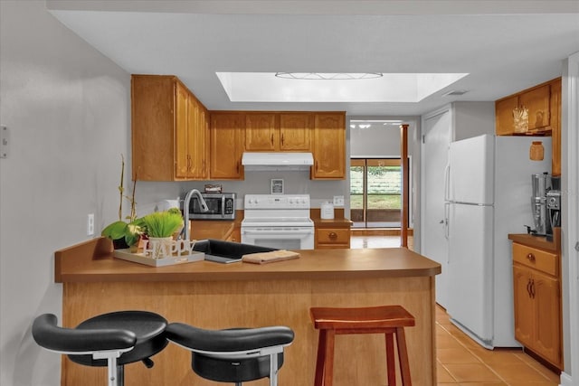 kitchen with a breakfast bar, white appliances, kitchen peninsula, and a skylight