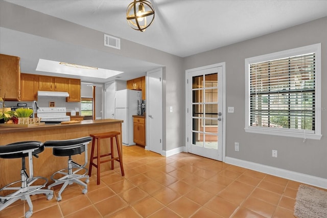 kitchen featuring a kitchen bar, kitchen peninsula, a wealth of natural light, and white appliances