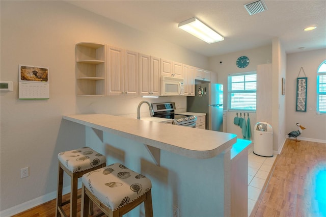 kitchen featuring kitchen peninsula, stainless steel appliances, a breakfast bar area, and light hardwood / wood-style flooring