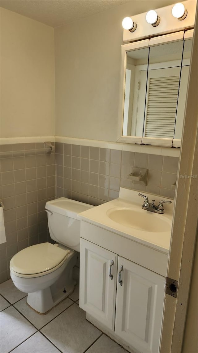 bathroom featuring tile patterned flooring, vanity, toilet, and tile walls