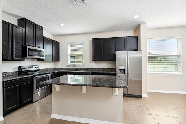 kitchen with appliances with stainless steel finishes, a kitchen breakfast bar, sink, dark stone countertops, and a center island