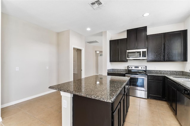 kitchen with stainless steel appliances, a kitchen island, dark stone counters, and light tile patterned flooring