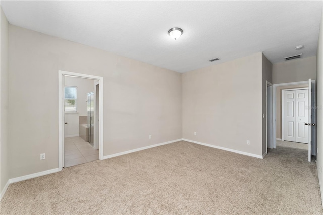 unfurnished bedroom with ensuite bathroom, light colored carpet, and a textured ceiling