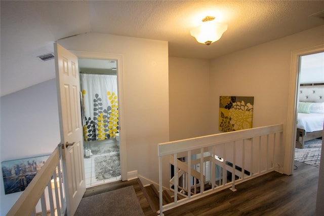 hallway with dark hardwood / wood-style flooring, a textured ceiling, and vaulted ceiling