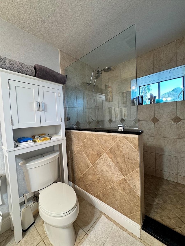 bathroom with tile patterned flooring, toilet, tiled shower, and a textured ceiling