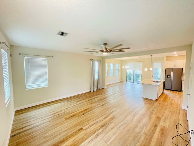 unfurnished living room with ceiling fan, light wood-type flooring, plenty of natural light, and sink