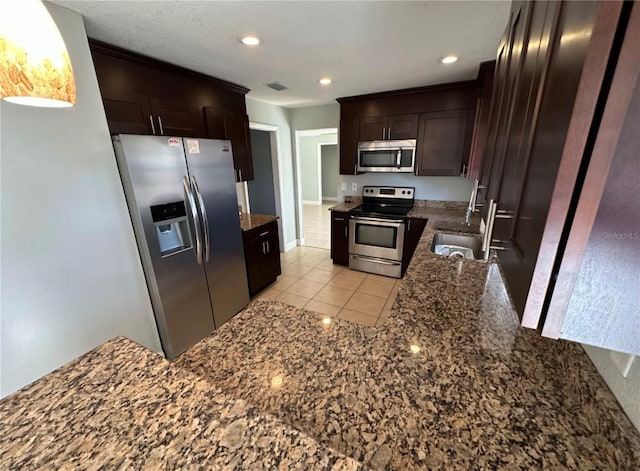 kitchen featuring dark stone counters, sink, light tile patterned floors, dark brown cabinets, and stainless steel appliances