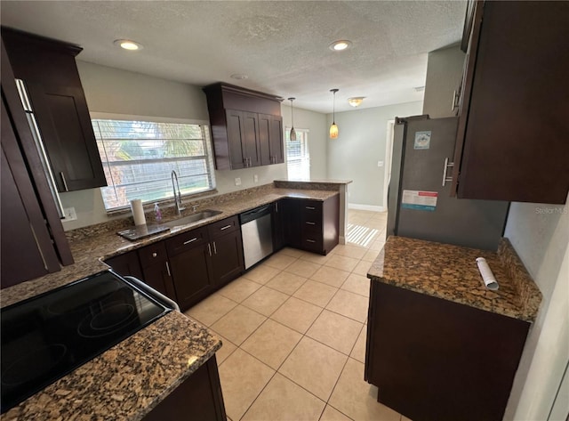 kitchen with kitchen peninsula, appliances with stainless steel finishes, a textured ceiling, decorative light fixtures, and light tile patterned flooring