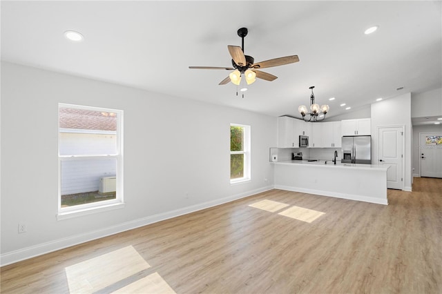 unfurnished living room with ceiling fan with notable chandelier, light hardwood / wood-style floors, vaulted ceiling, and sink