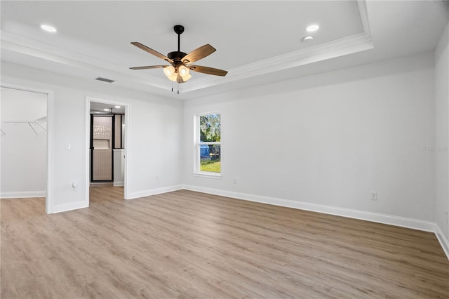 empty room with ceiling fan, light wood-type flooring, crown molding, and a tray ceiling