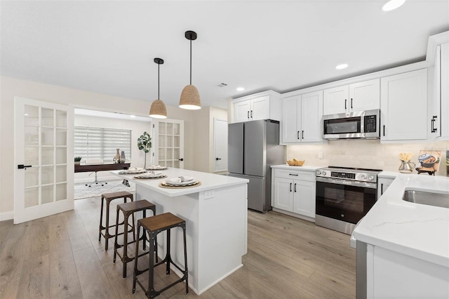 kitchen featuring light stone countertops, appliances with stainless steel finishes, backsplash, white cabinetry, and hanging light fixtures