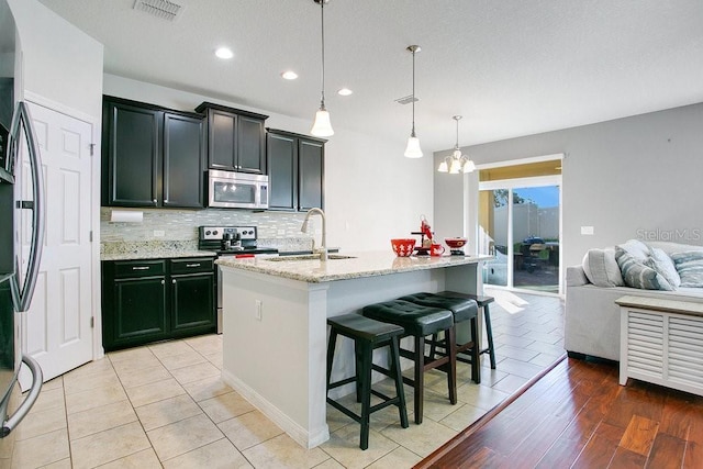 kitchen with pendant lighting, a kitchen island with sink, sink, appliances with stainless steel finishes, and light hardwood / wood-style floors