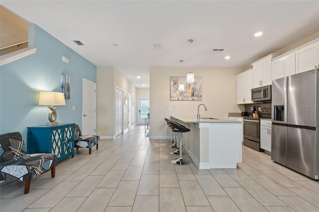 kitchen featuring white cabinetry, an island with sink, decorative light fixtures, a kitchen bar, and appliances with stainless steel finishes