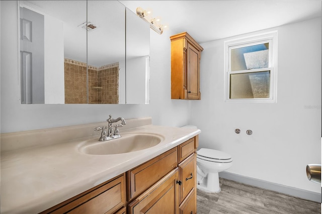 bathroom featuring tiled shower, hardwood / wood-style floors, vanity, and toilet