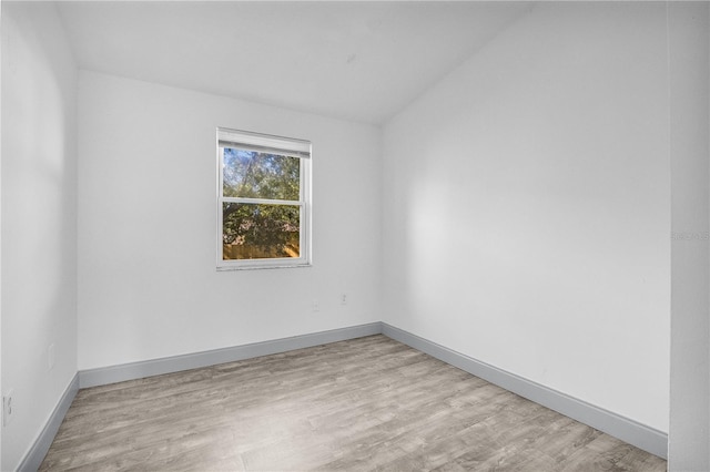 spare room with light wood-type flooring and lofted ceiling