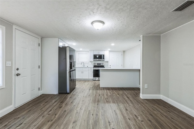 kitchen with appliances with stainless steel finishes, a textured ceiling, sink, dark hardwood / wood-style floors, and white cabinetry