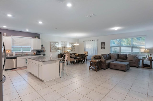 kitchen featuring a breakfast bar, white cabinets, stainless steel dishwasher, dark stone countertops, and a kitchen island