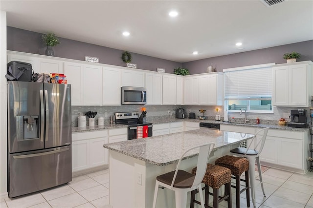 kitchen with a center island, white cabinets, sink, appliances with stainless steel finishes, and a kitchen bar