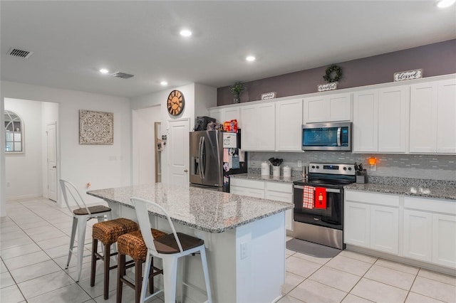 kitchen featuring white cabinetry, stainless steel appliances, light stone counters, backsplash, and a kitchen island