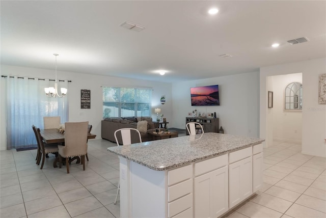 kitchen featuring pendant lighting, an island with sink, light stone counters, white cabinetry, and a chandelier