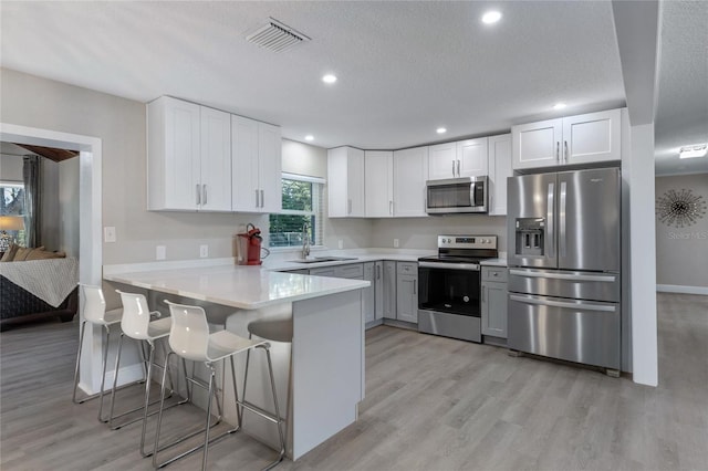 kitchen featuring kitchen peninsula, a breakfast bar, stainless steel appliances, sink, and white cabinetry