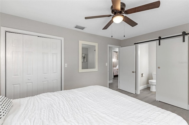 bedroom with ceiling fan, a barn door, hardwood / wood-style flooring, connected bathroom, and a closet