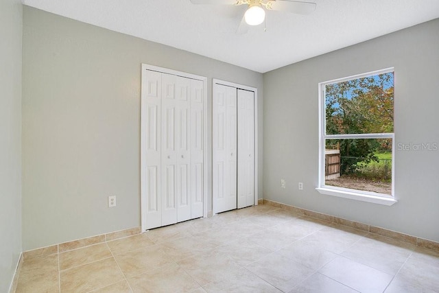 unfurnished bedroom with light tile patterned floors, two closets, and ceiling fan